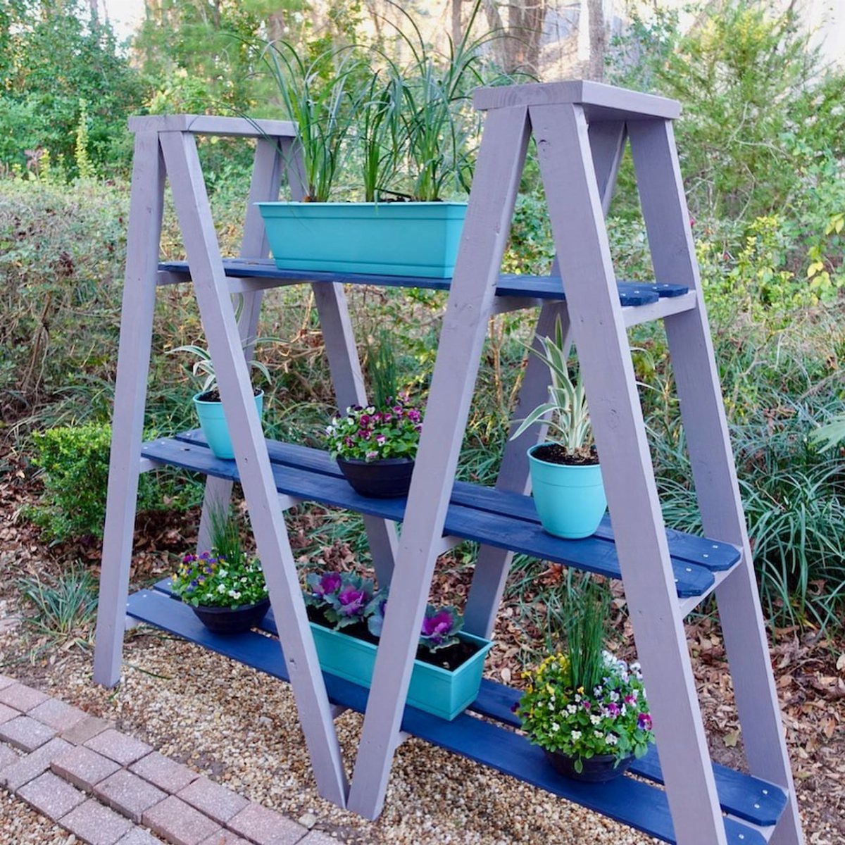 2x4 Plant Stand Ideas: 6 Builds for Indoors and Out 3 Double ladder plant stand painted grey and blue with various potted flowers outdoors.