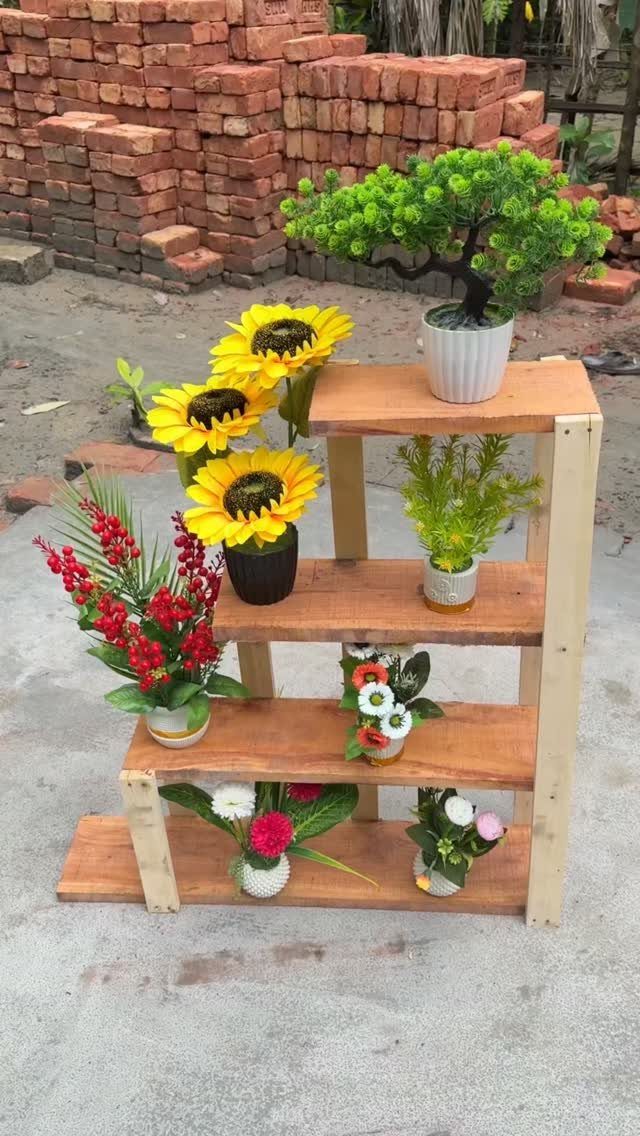 2x4 Plant Stand Ideas: 6 Builds for Indoors and Out 1 Four-tiered wooden plant stand holding various colorful potted plants against a brick wall.