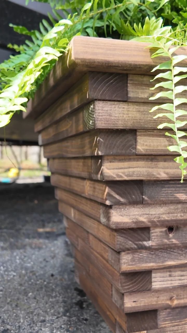 2x4 Plant Stand Ideas: 6 Builds for Indoors and Out 4 Stacked dark brown 2x4 wooden planter box with green ferns growing from the top.