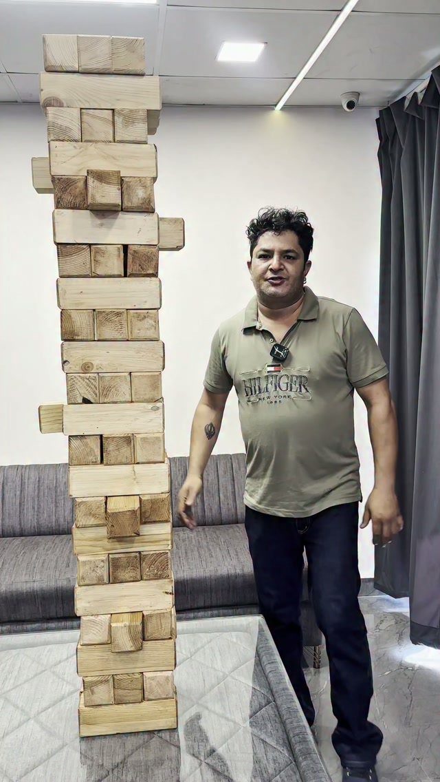 Giant Jenga tower of wooden blocks standing next to a man in a room.
