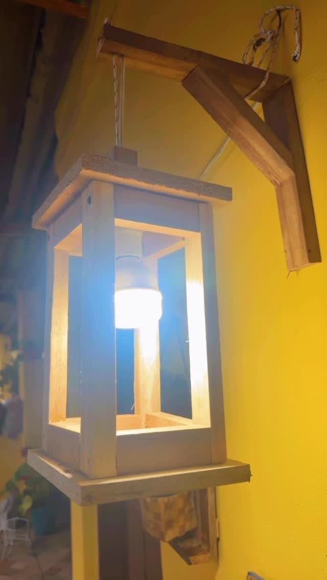 Wooden lantern with a glowing light bulb hanging from a wall bracket.