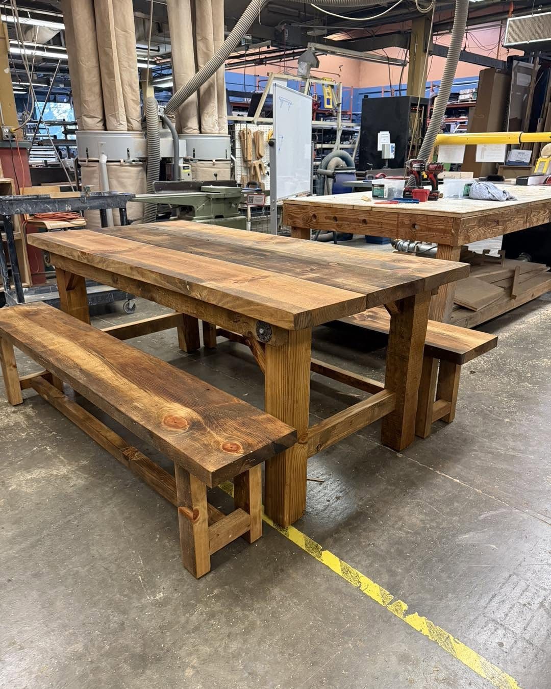 Rustic wooden dining table and matching benches in a woodworking shop setting.