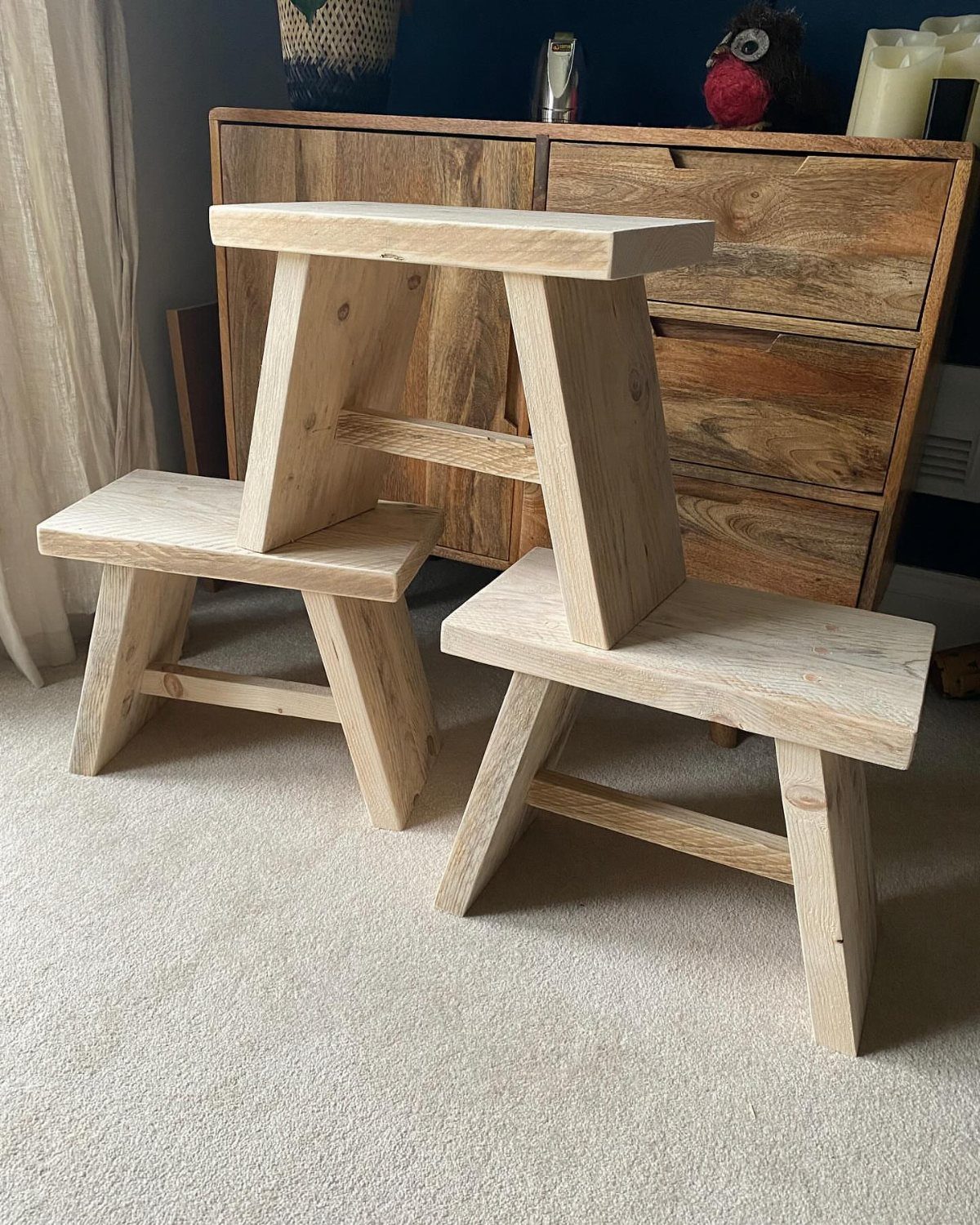 Two light wood step stools standing on a carpeted floor indoors.