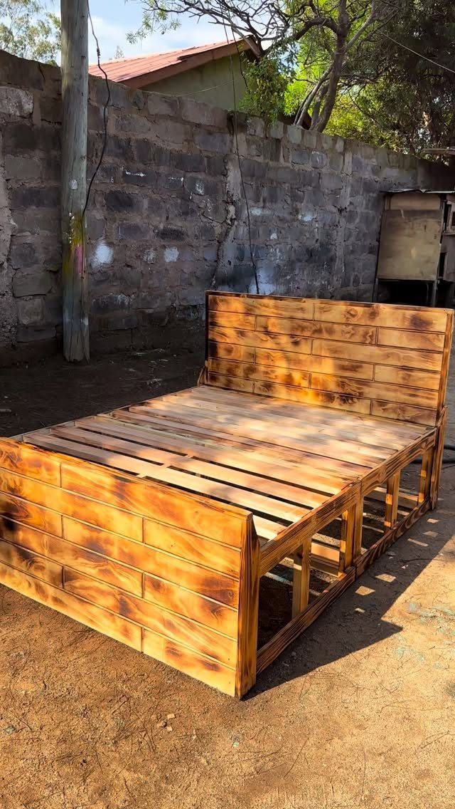 What Can You Do With Burned and Stained Wood? 5 Ideas 4 Wooden pallet bed frame with charred edges and golden brown stain outdoors.