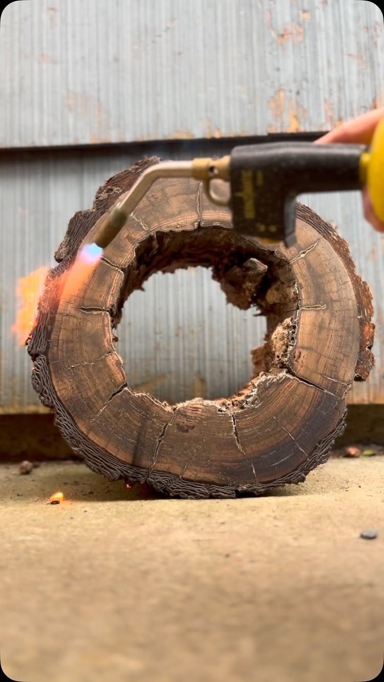 Burned Wood Finish Ideas: 8 Charred Projects for Home 1 Handheld torch burning the edge of a circular wooden slab outdoors.