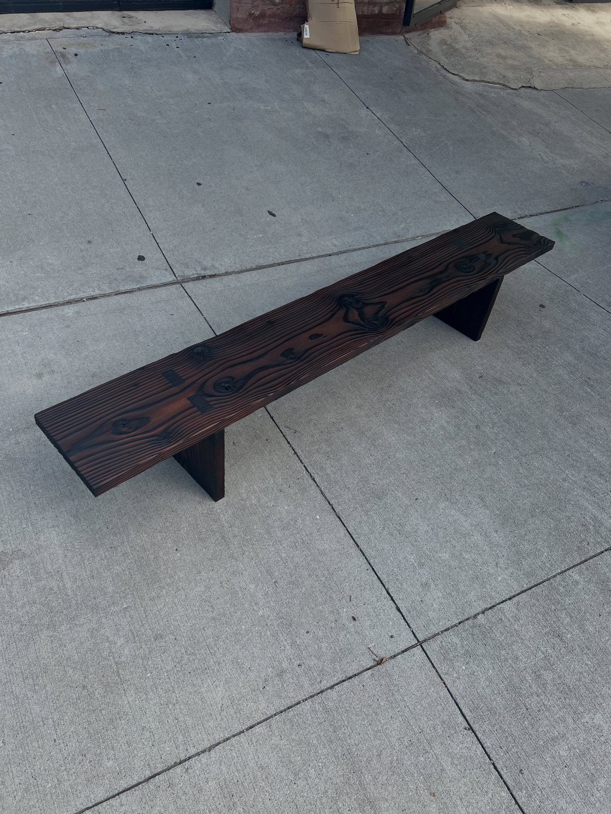 Burned Wood Finish Ideas: 8 Charred Projects for Home 3 Charred black wooden bench with visible grain on a grey concrete sidewalk