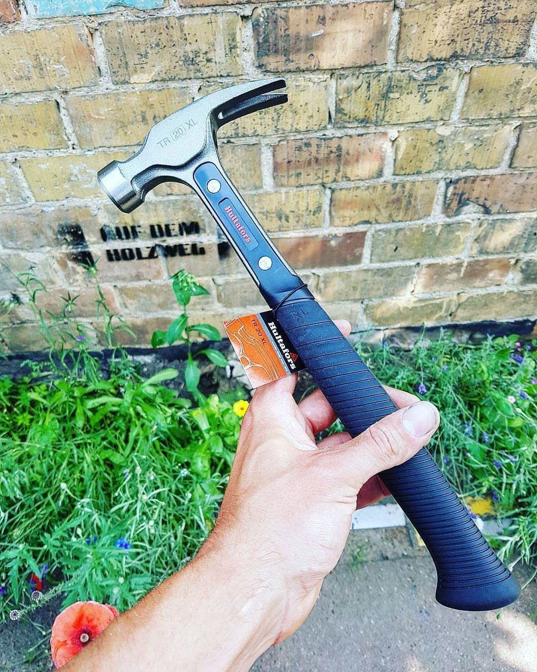 Carpenter Tools with Name: 7 Basics for Every Toolbox 1 Claw hammer with black grip held by a hand against a brick wall.
