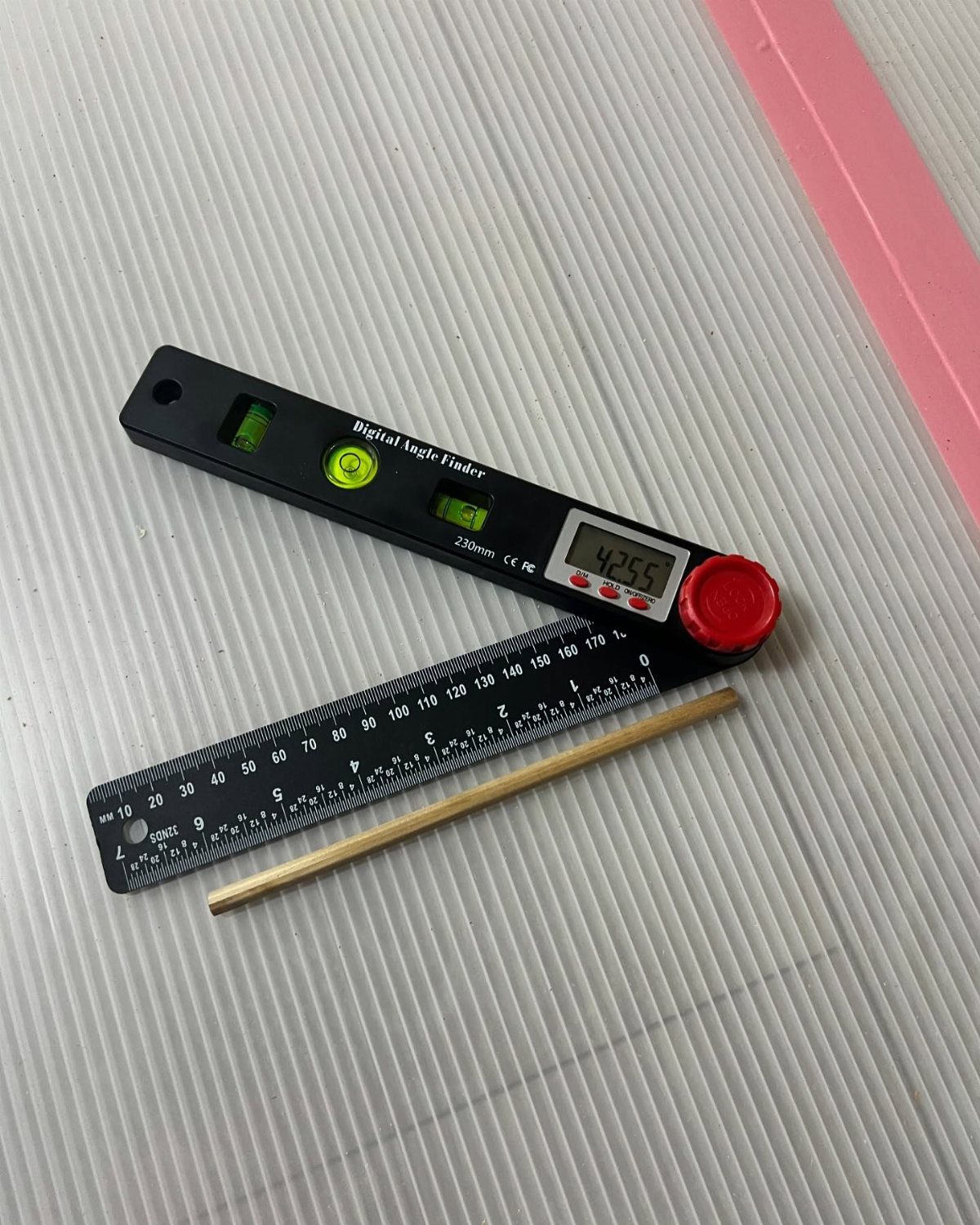 Carpenter Tools with Name: 7 Basics for Every Toolbox 7 Digital angle finder, metal ruler, and brass rod on a white ribbed surface.