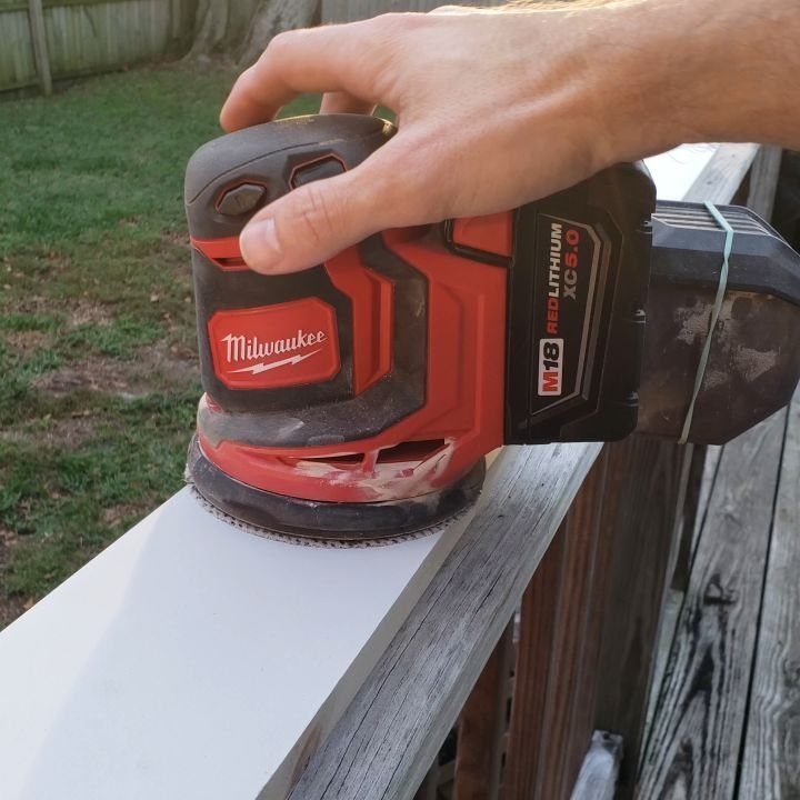 Carpenter Tools with Name: 7 Basics for Every Toolbox 5 Red cordless power sander being used to smooth a white wooden railing outdoors.