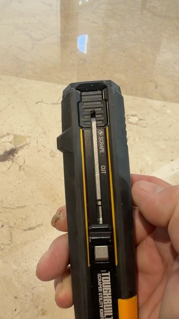 Carpenter Tools with Name: 7 Basics for Every Toolbox 3 Black and yellow utility knife held by a hand against a marble surface.