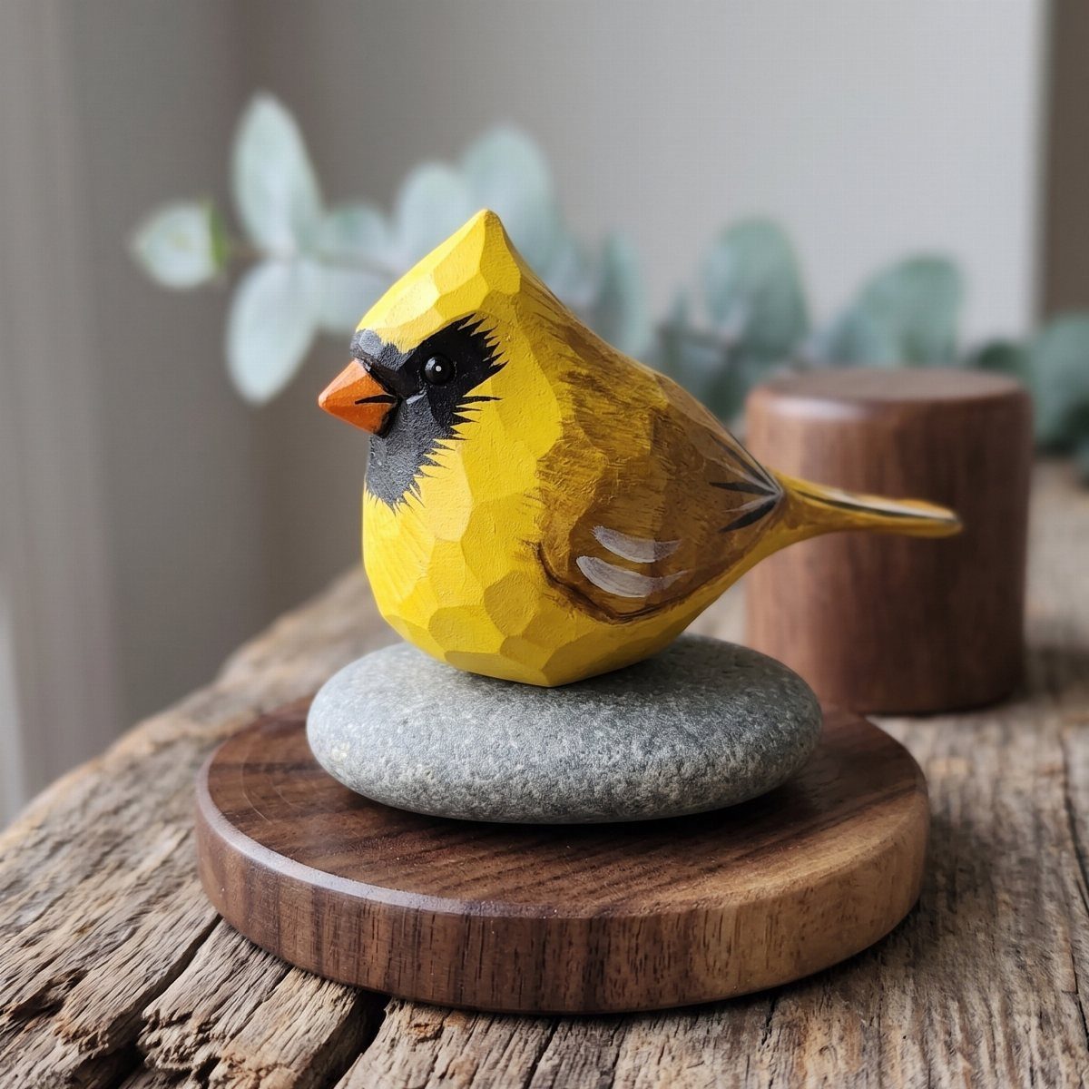 Yellow carved wooden bird resting on a grey stone and wooden base.