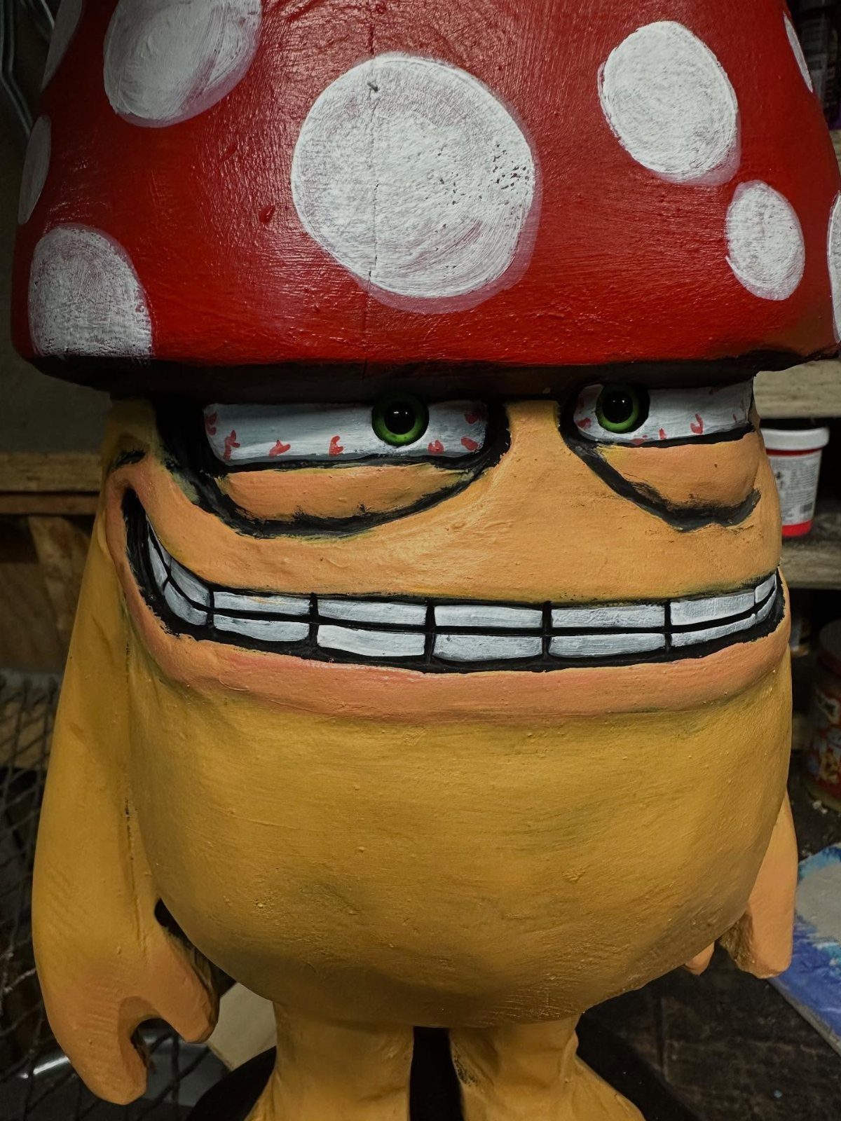 Carved wooden figure of a yellow character wearing a red spotted mushroom cap