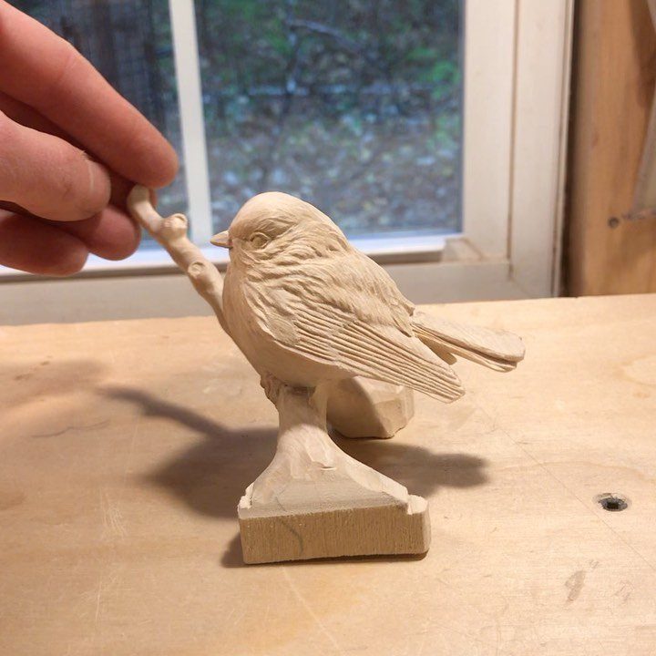 Wooden bird carving perched on a branch resting on a light wood workbench