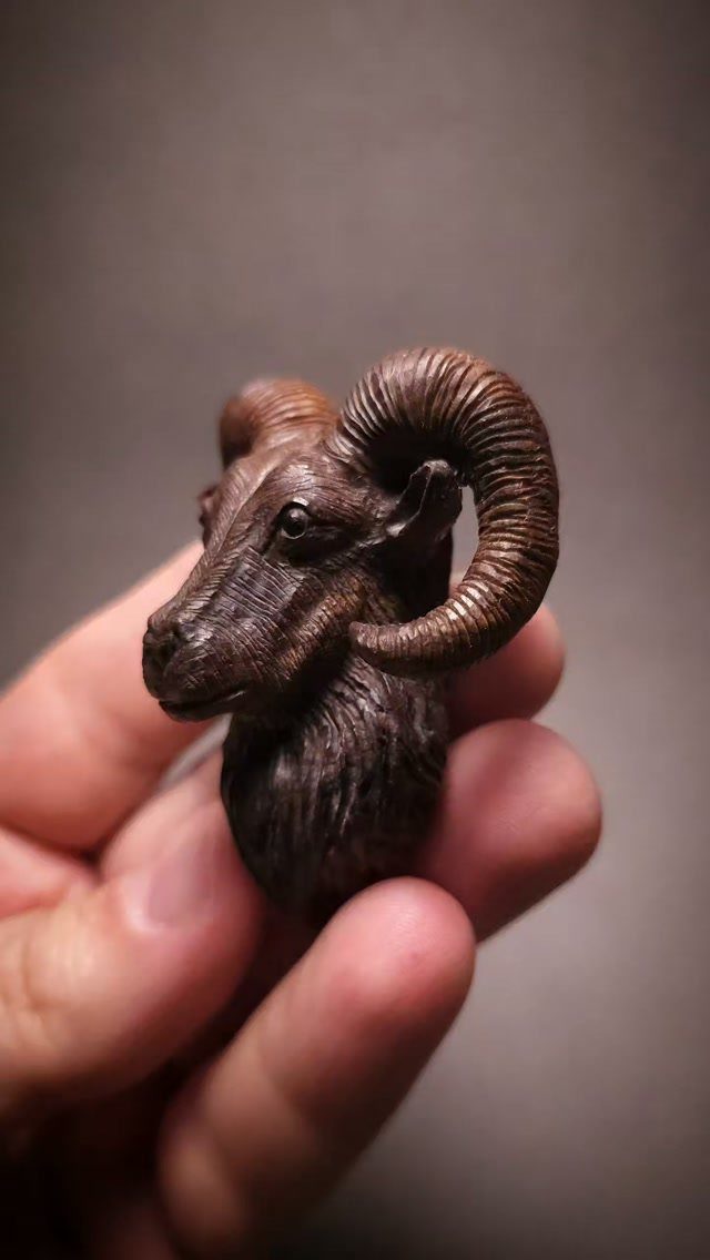 Small wooden carving of a ram's head held in a person's hand.