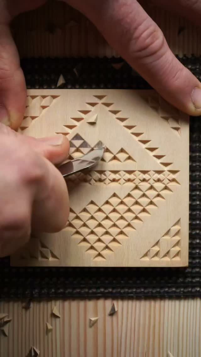 Hands carving intricate geometric patterns into a light-colored square wooden block.