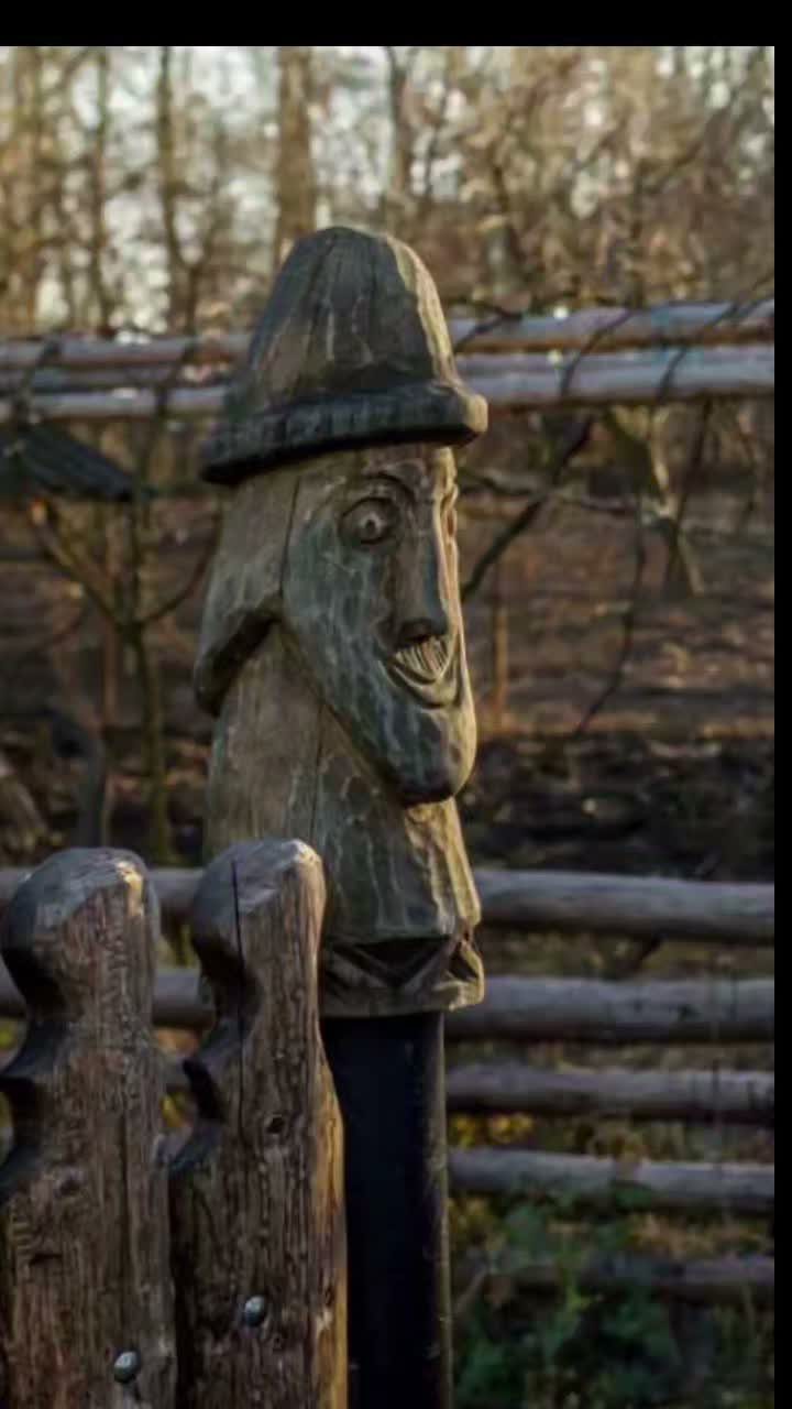 Carved wooden figure of a smiling person with a hat on a post.