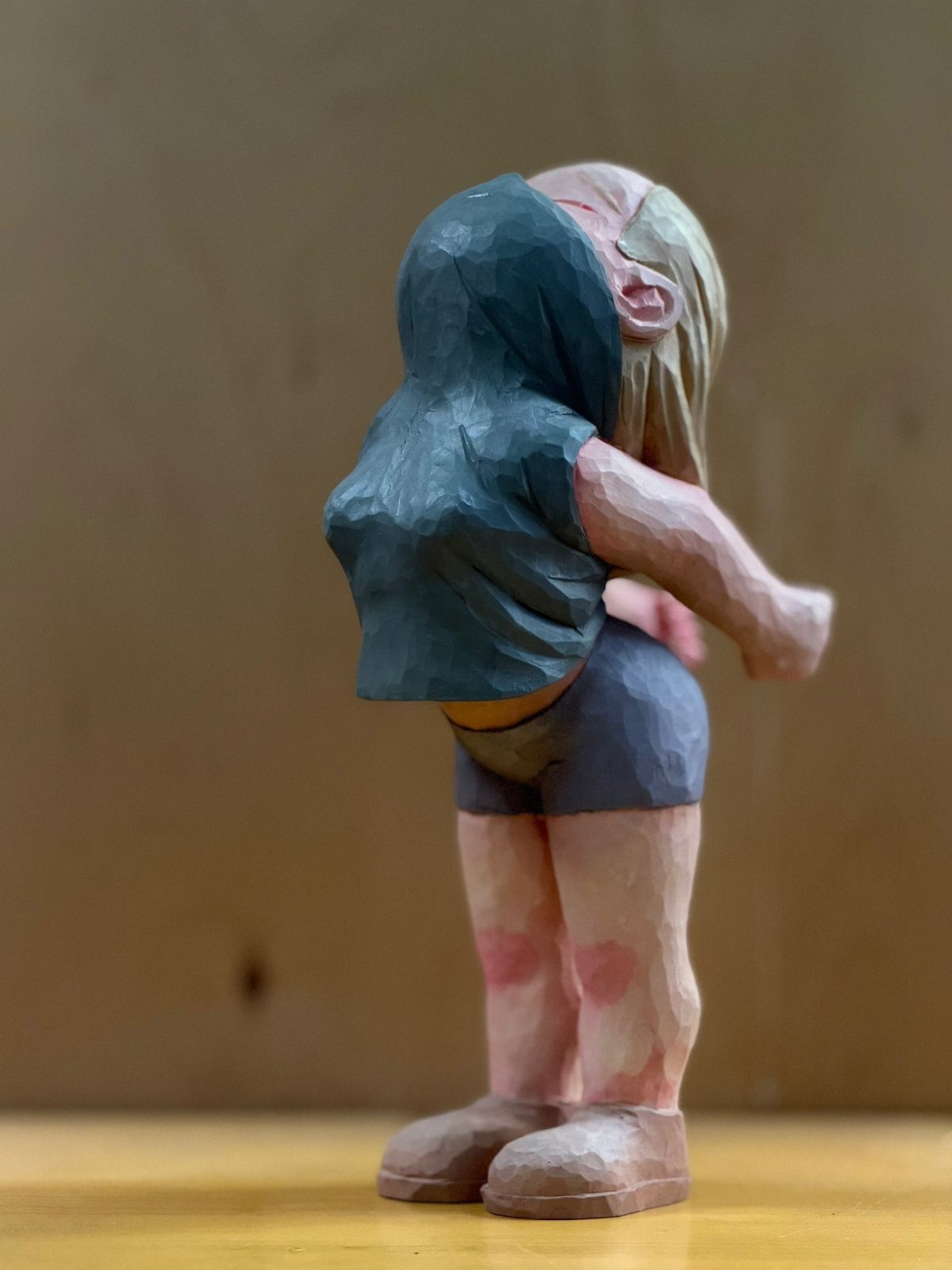 Hand-carved wooden figure of a person in a blue vest and grey shorts.