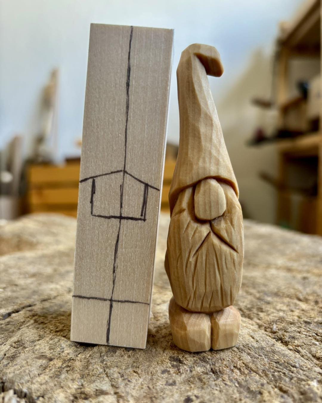 Carved wooden gnome figure standing beside a wood block with a pencil sketch.