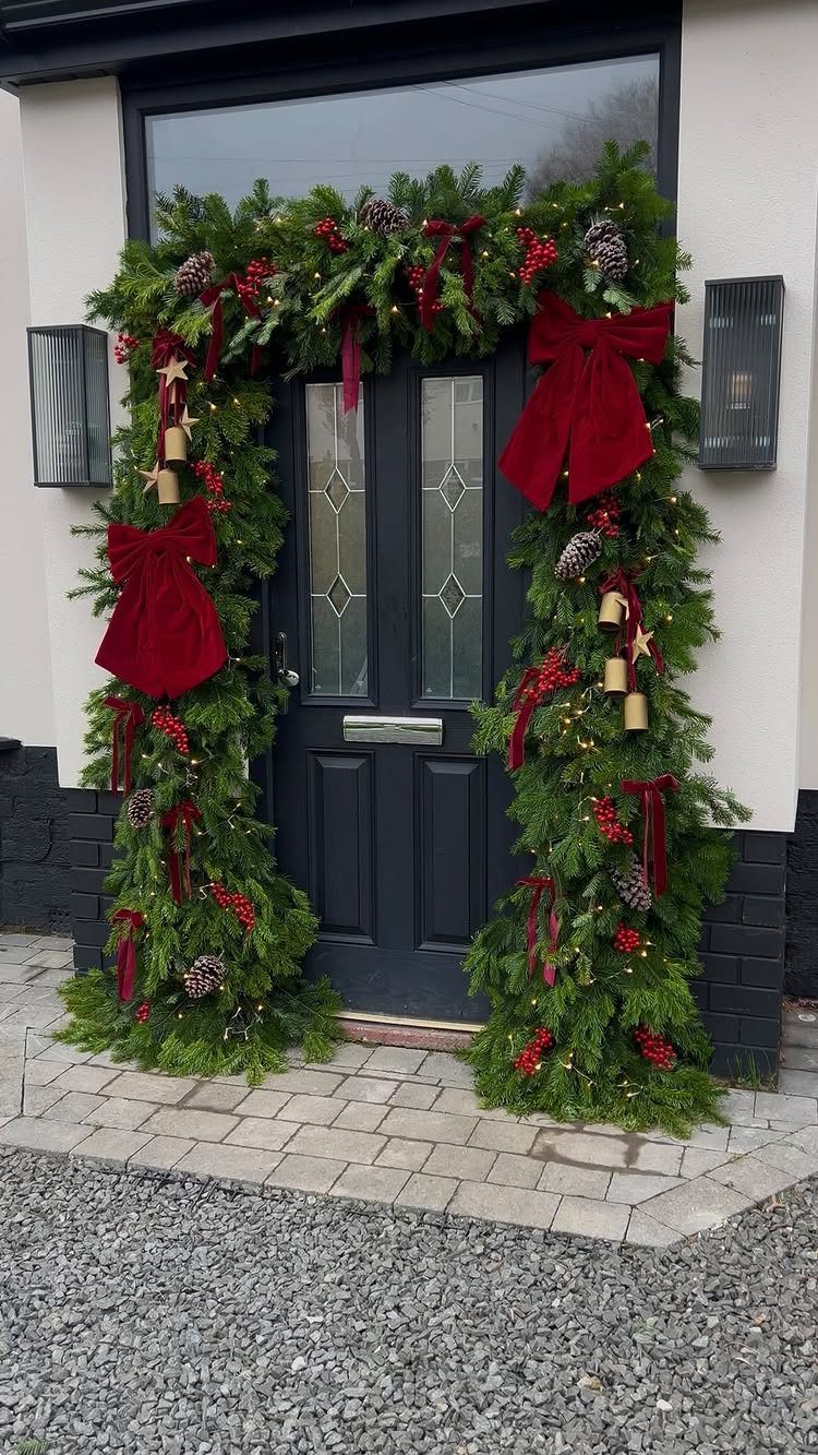 12 Christmas Decorations DIY for Outdoor Spaces 8 Evergreen garland with red bows and fairy lights framing a dark grey front door.