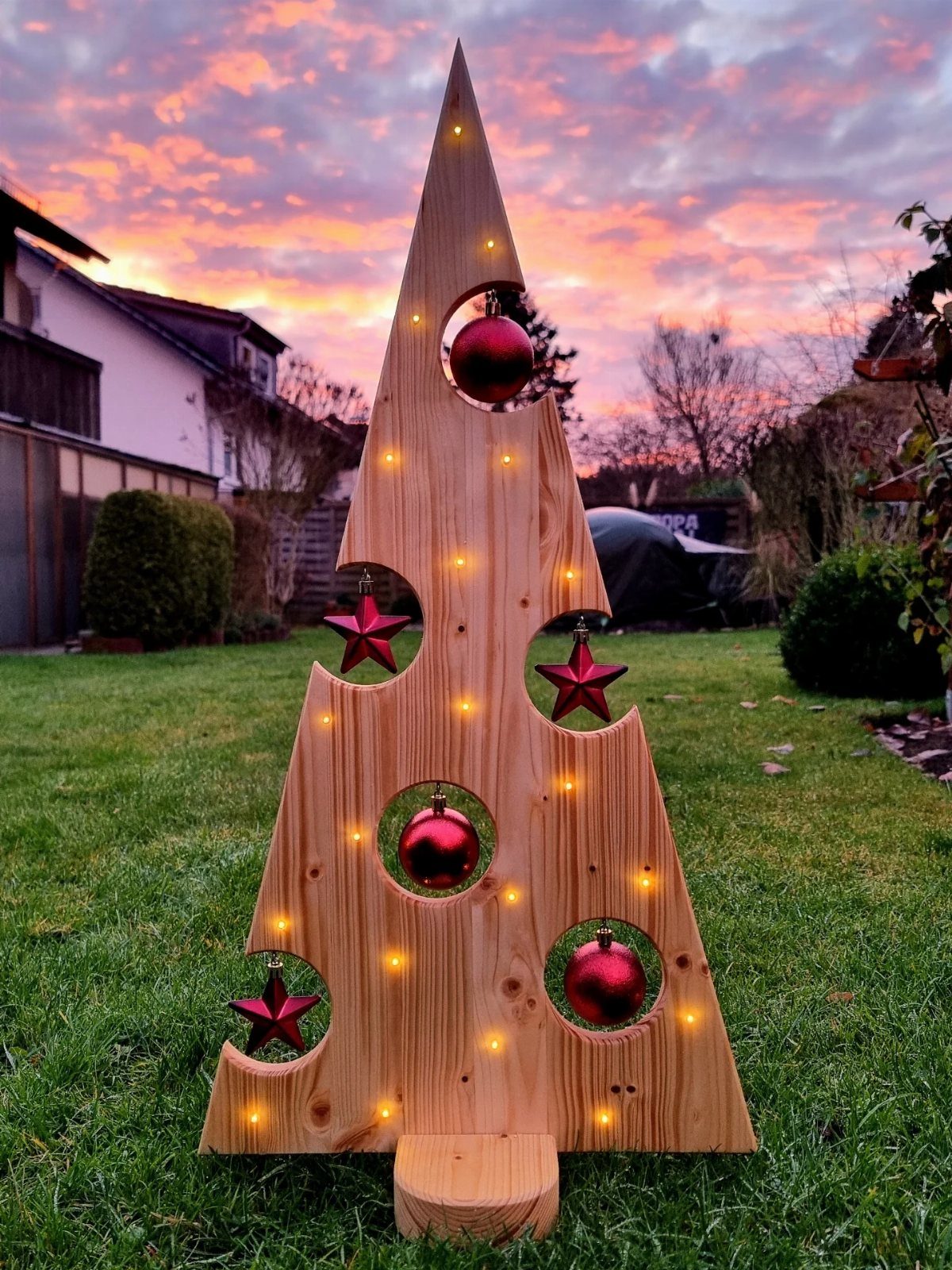 12 Christmas Decorations DIY for Outdoor Spaces 9 Wooden Christmas tree decoration with red ornaments and lights on a green lawn