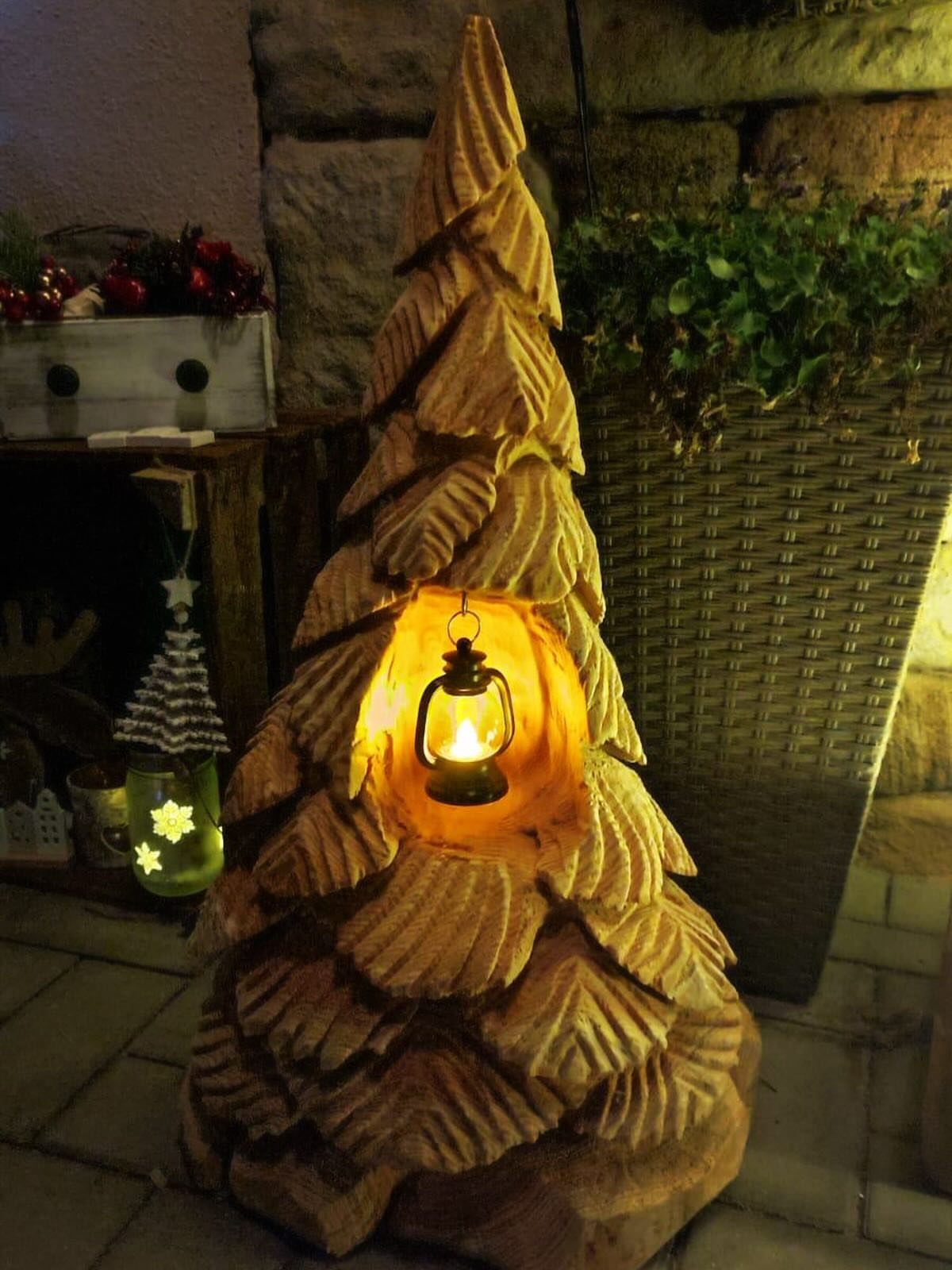 12 Christmas Decorations DIY for Outdoor Spaces 7 Carved wooden Christmas tree sculpture with a glowing lantern inside on a porch.