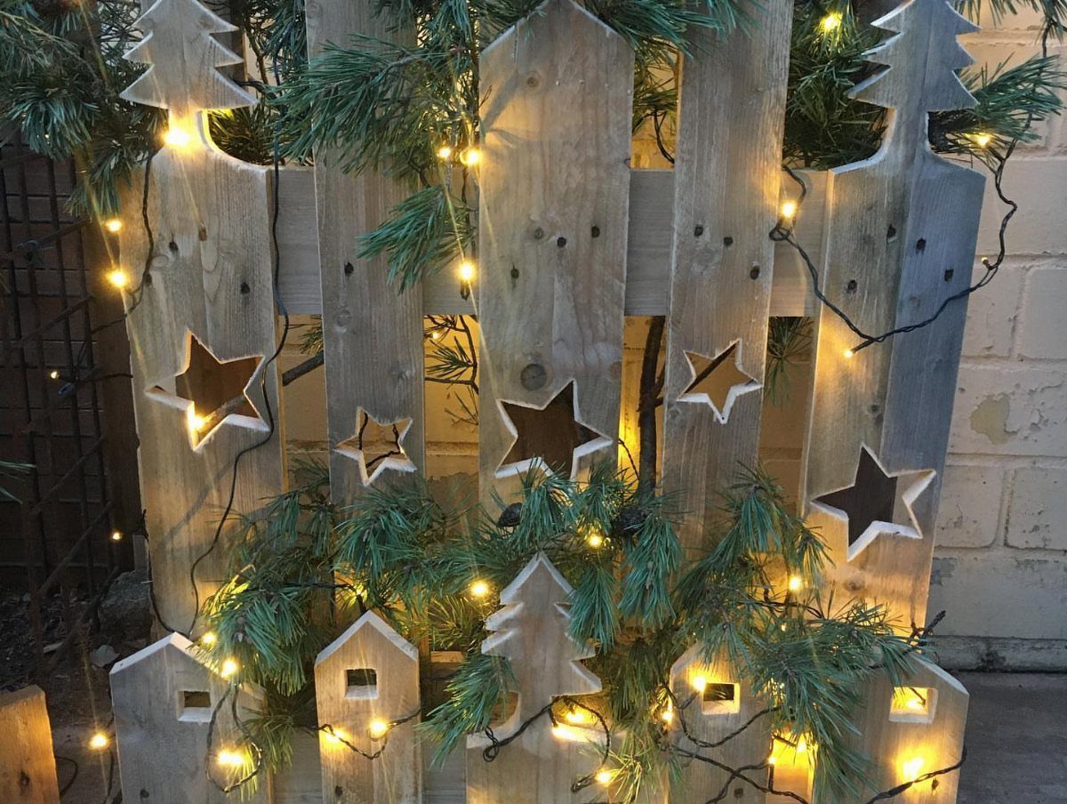 8 Christmas Pallet Projects for Holiday Decor 7 Rustic wooden pallet decoration with star cut-outs, pine branches, and glowing fairy lights.