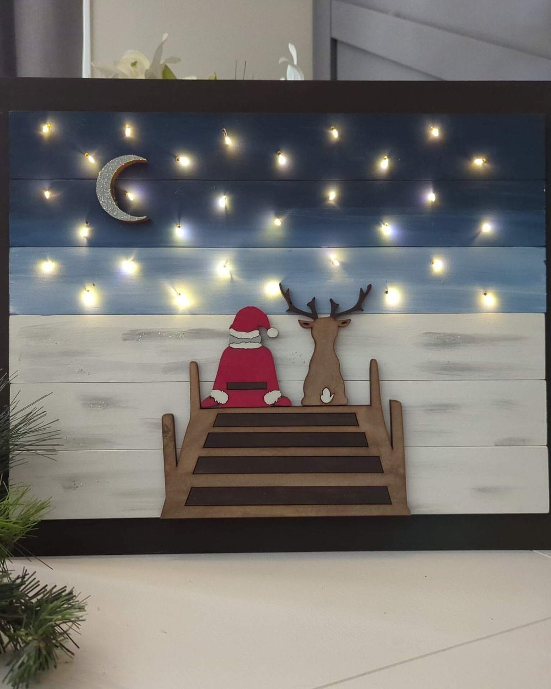 8 Christmas Pallet Projects for Holiday Decor 6 Santa and a reindeer sitting on a wooden bench under a starry night sky.