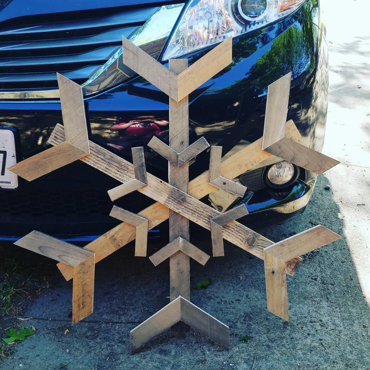 8 Christmas Pallet Projects for Holiday Decor 4 Wooden pallet snowflake decoration leaning against the front of a black car.