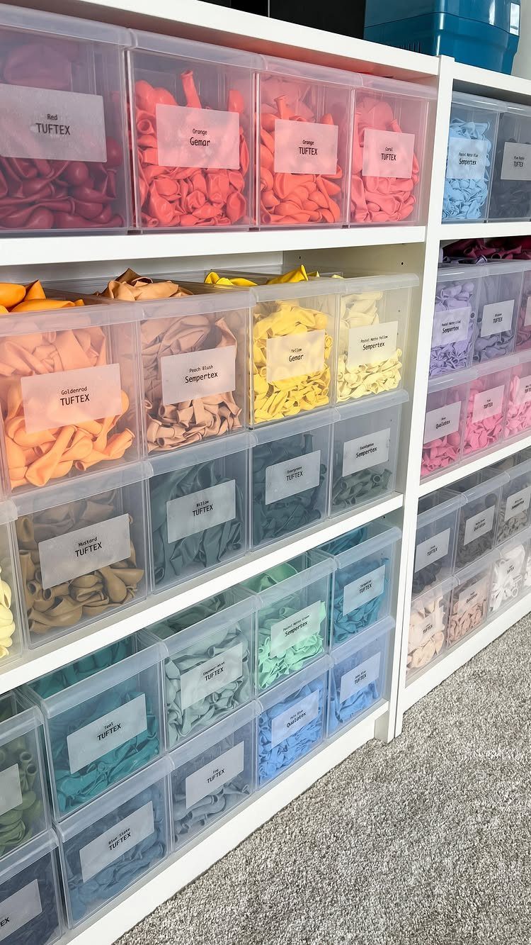 Clear plastic storage bins filled with colorful craft materials on white shelving units.