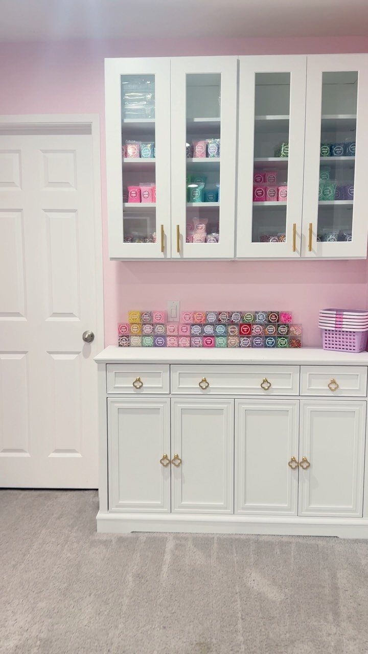 White storage cabinets and sideboard with colorful organized craft supplies against pink walls