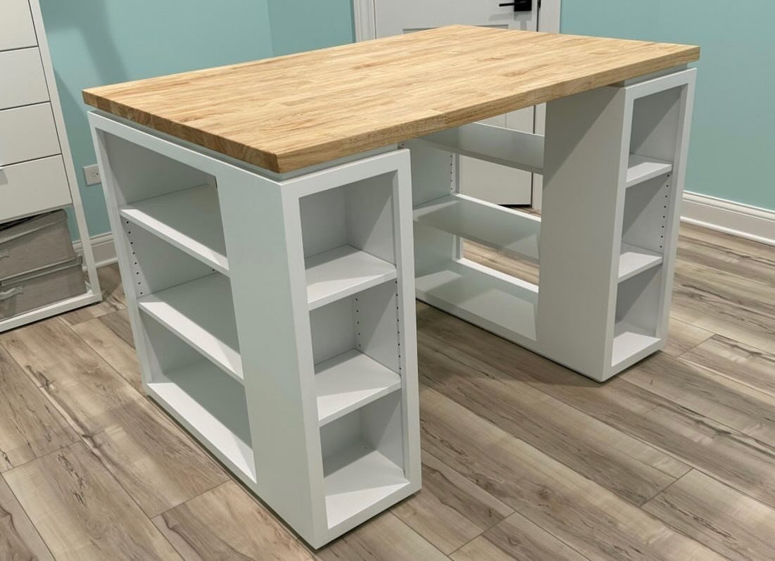 Custom craft table with a wooden top and white shelving unit supports.