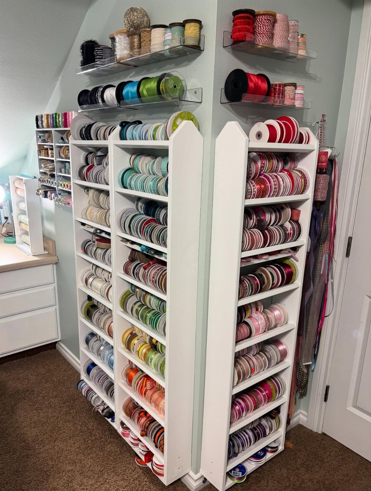 White wooden shelving units and acrylic wall shelves filled with colorful ribbon spools.