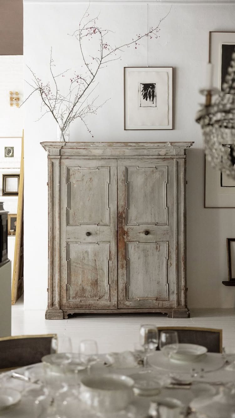 Weathered light-grey wooden armoire standing against a white wall in a dining room.
