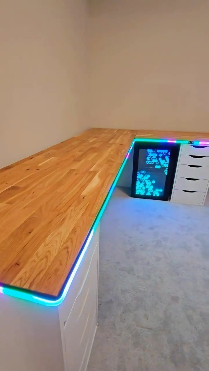 L-shaped wooden gaming desk with white drawers and cyan LED under-glow lighting.