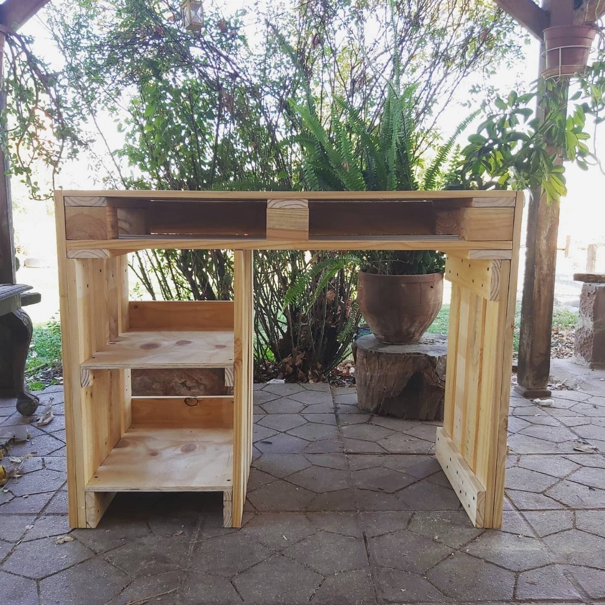 Handmade wooden desk with side shelving standing on a stone patio outdoors.