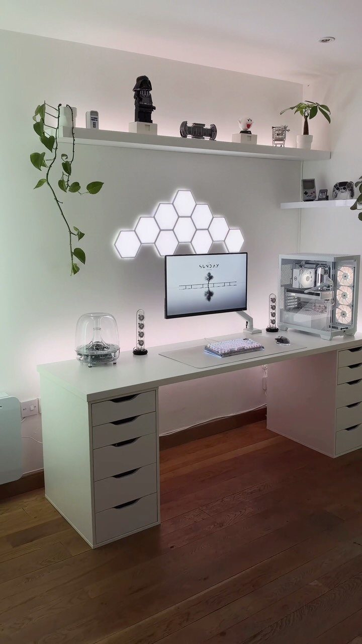 White gaming desk setup with hexagonal wall lights, monitor, and PC tower.