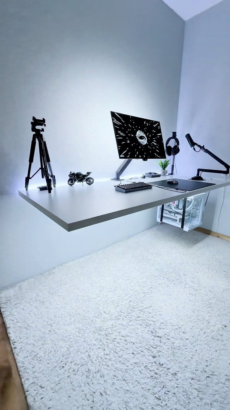 White floating desk mounted to a wall with a gaming computer setup and tripod.