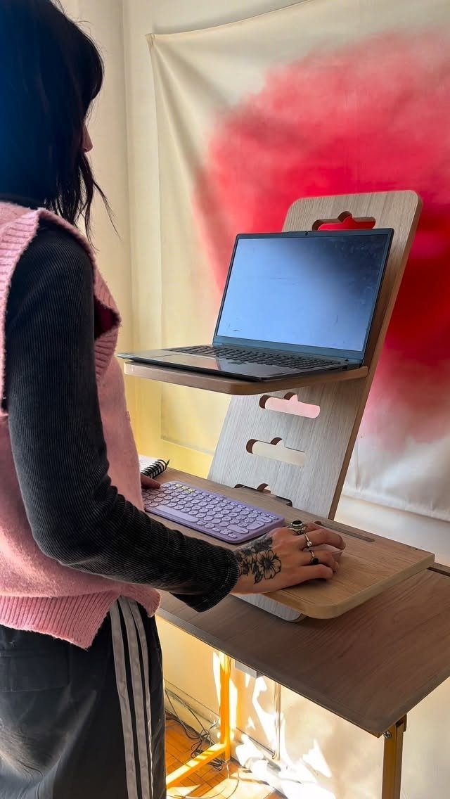 Standing desk converter holding a laptop and keyboard on a wooden table.