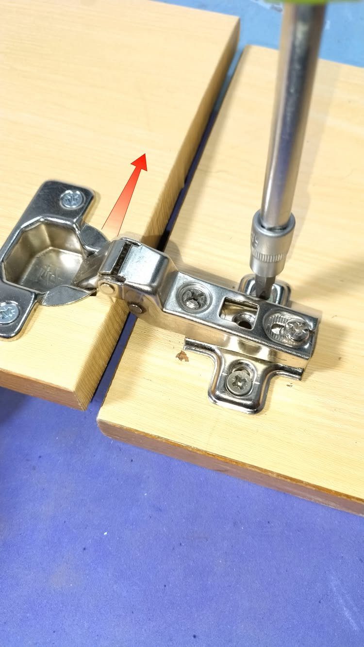 Metal cabinet hinge being installed on light wood with a screwdriver