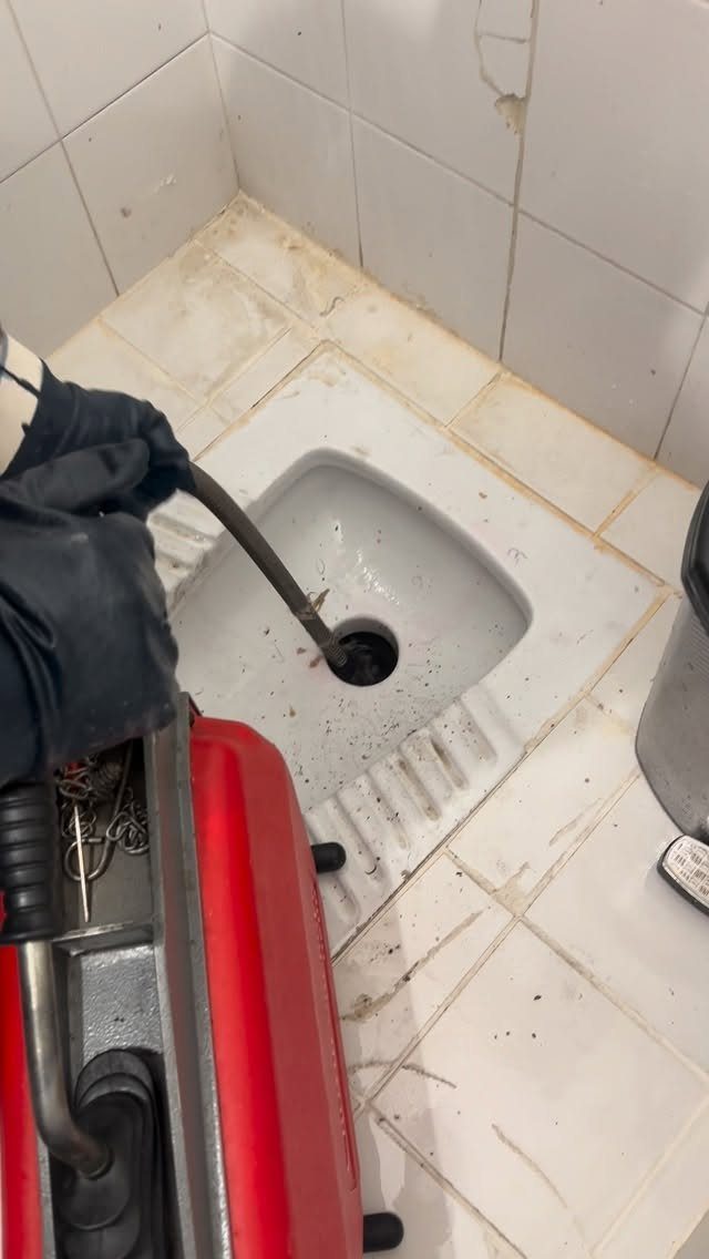 Person using a red vacuum hose to unclog a white tiled shower drain.