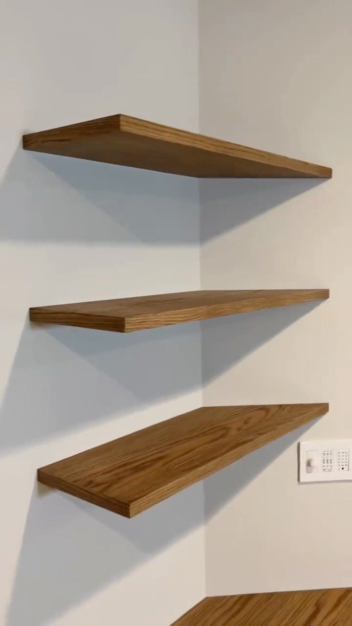 Three natural wood floating shelves mounted on a clean white wall corner.