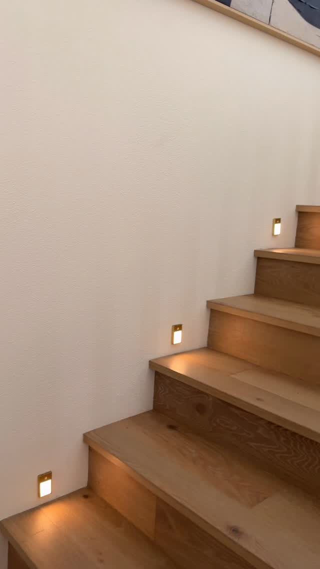 Wooden stairs with small square recessed wall lights illuminating each step.