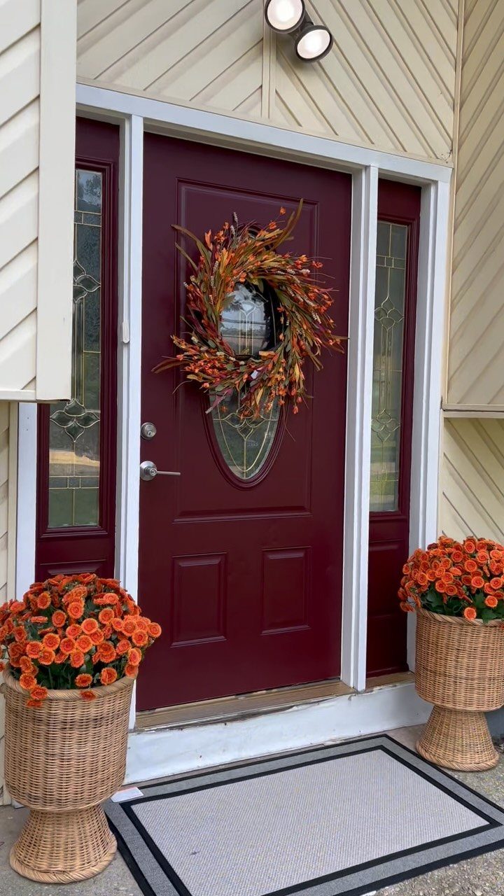 Deep red painted front door with an autumn wreath and orange flower planters.