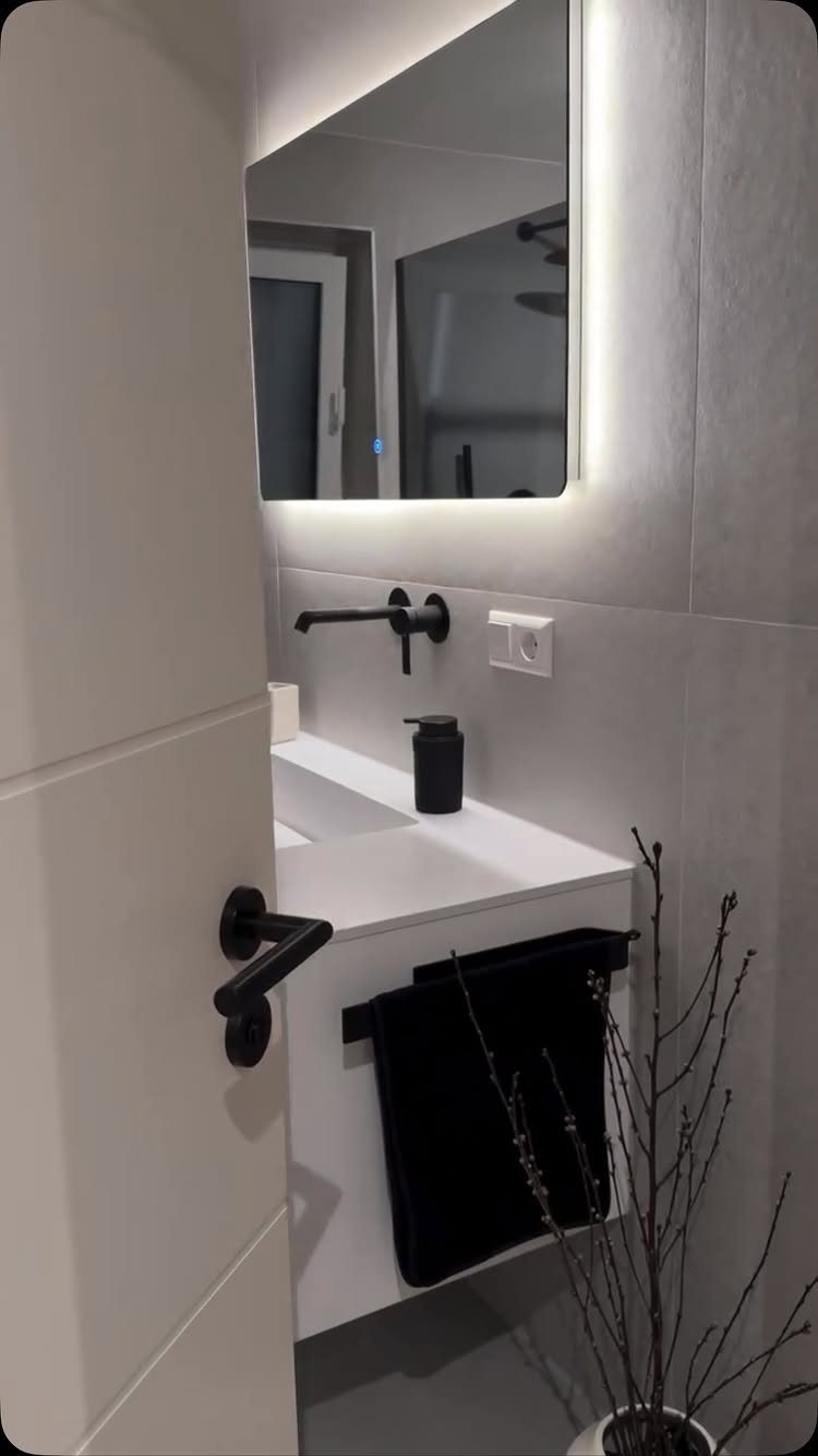 Modern white floating sink with a matte black wall-mounted faucet and backlit mirror.