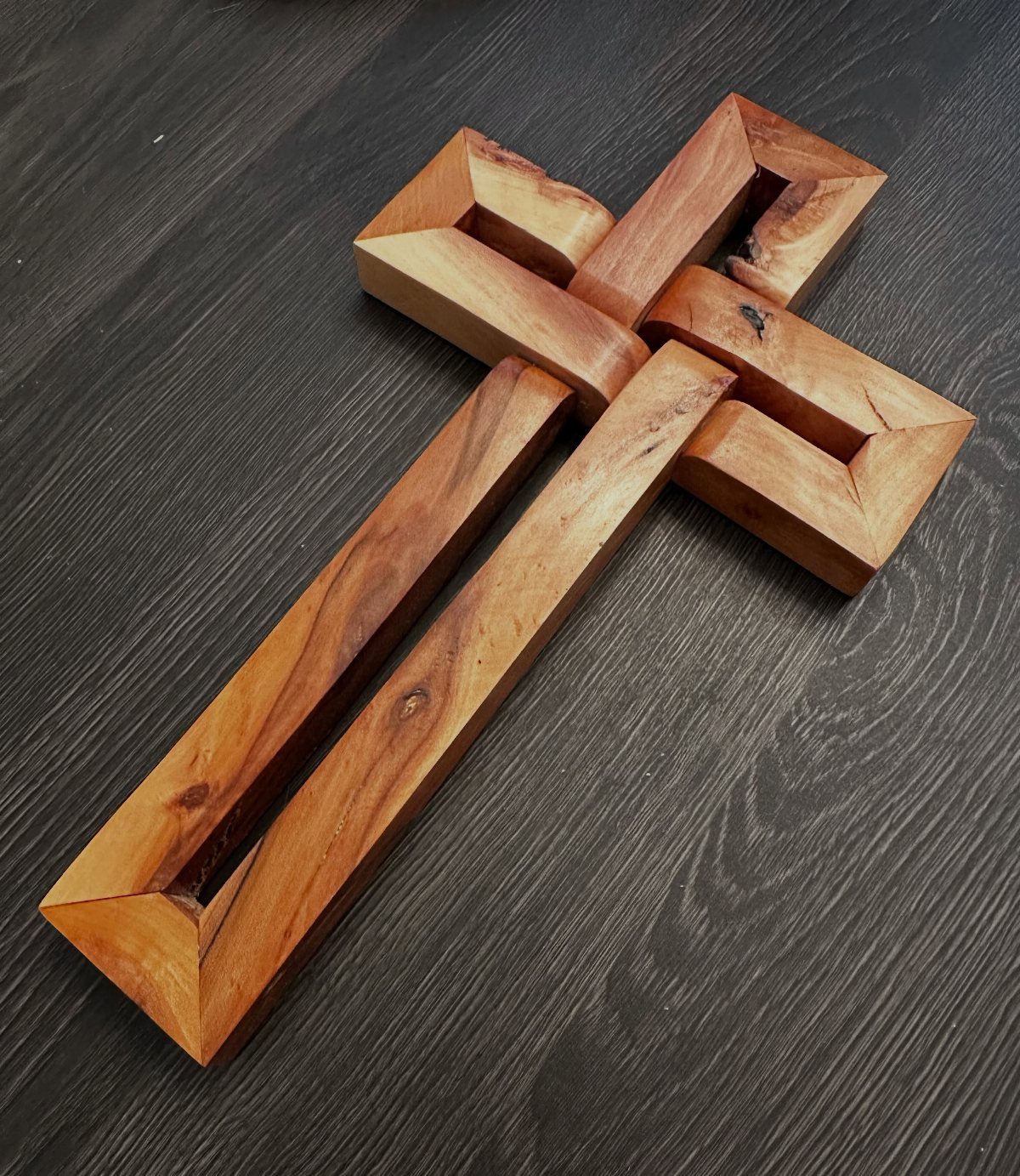 DIY Wooden Crosses: 5 Ideas, from Woven to Carved 1 Wooden woven infinity cross made of light brown wood on a dark surface