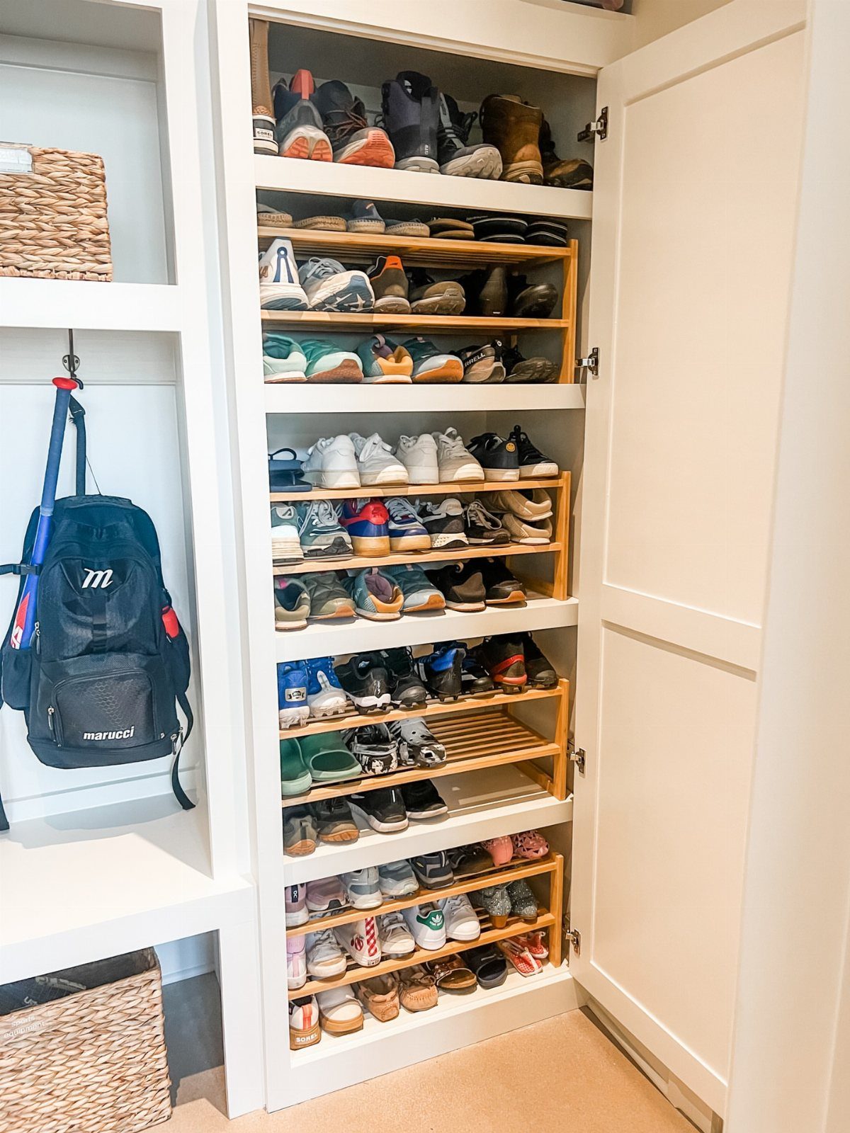 Built-in white closet with wooden shelves holding a variety of organized shoes.
