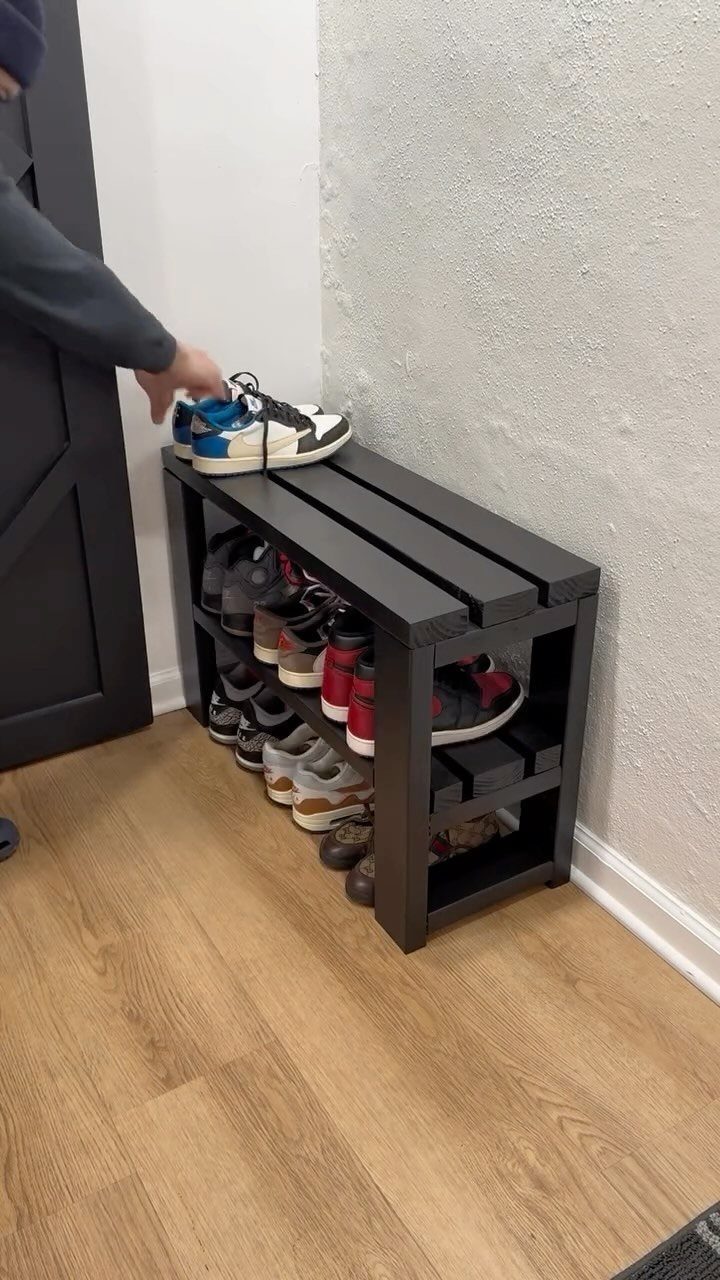 Dark grey wooden shoe storage bench filled with sneakers against a white wall.