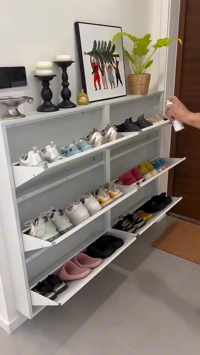 White wooden shoe storage cabinet with pull-out trays filled with various footwear.