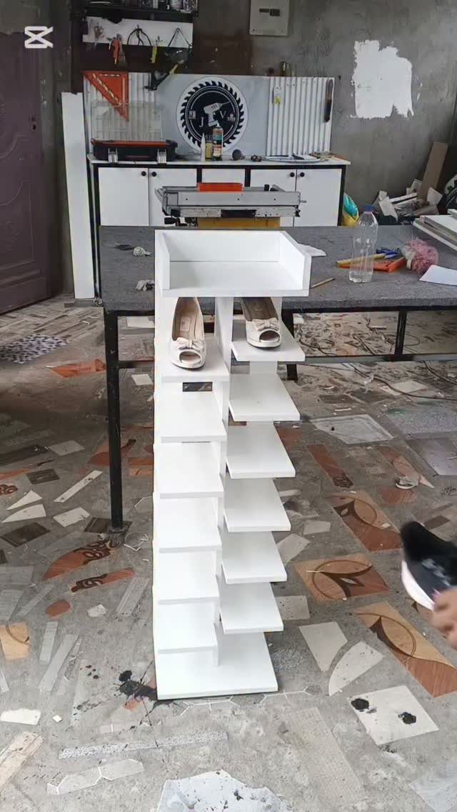 White wooden shoe rack with staggered shelves holding beige high heels in a workshop