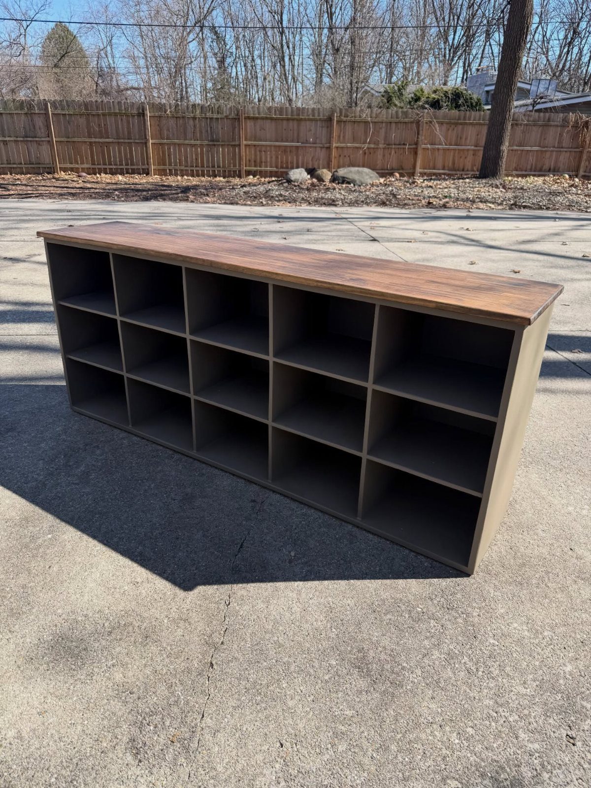 Wooden shoe rack with grey cubbies and a brown top on a concrete driveway.
